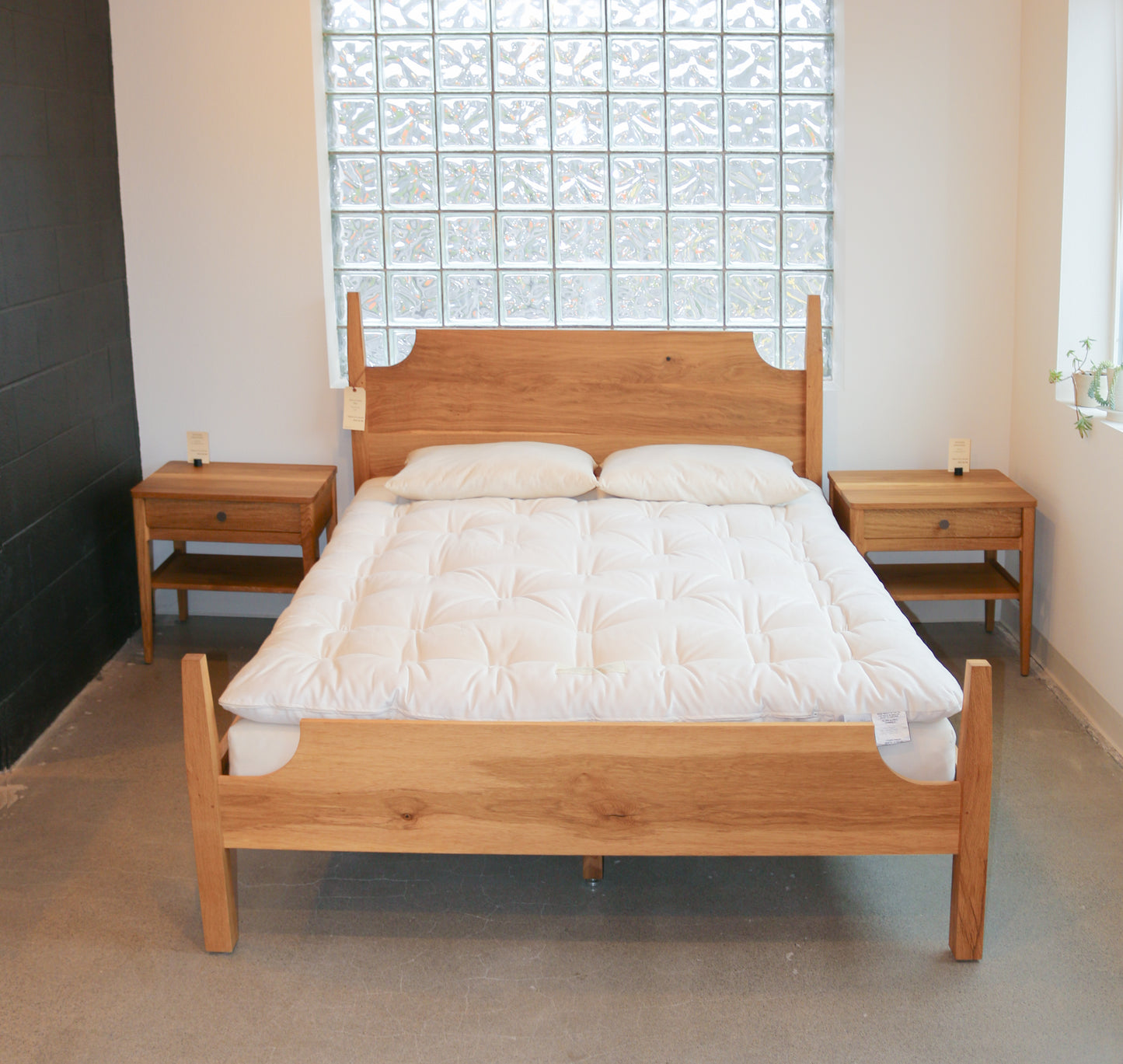 Wooden bed with white mattress in a room with a stained glass window.