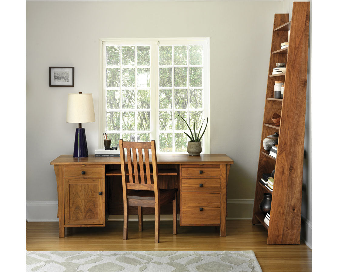 Wooden desk with chair in a home office setting with a bookshelf and window.