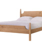 A light oak wood bed frame with a curved headboard and footboard, styled with white bedding and two pillows, isolated on a white background.