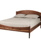 A dark Walnut wood platform bed frame with a curved headboard and footboard, shown with beige bedding and two pillows on a solid white background.