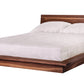 A modern low-profile platform bed with a dark Walnutwood frame and headboard, dressed in white bedding and two white pillows, shown against a plain white background.