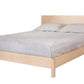 A light natural wood platform bed frame with a matching headboard, dressed in gray bedding and two gray pillows, shown against a plain white background.