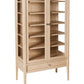 A tall, light natural oak wooden bookcase with two glass doors, multiple interior shelves, and a single drawer at the bottom, shown on a plain white background.