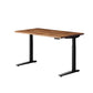 An adjustable height standing desk with a medium brown wood grain top and black metal legs, shown on a solid white background.
