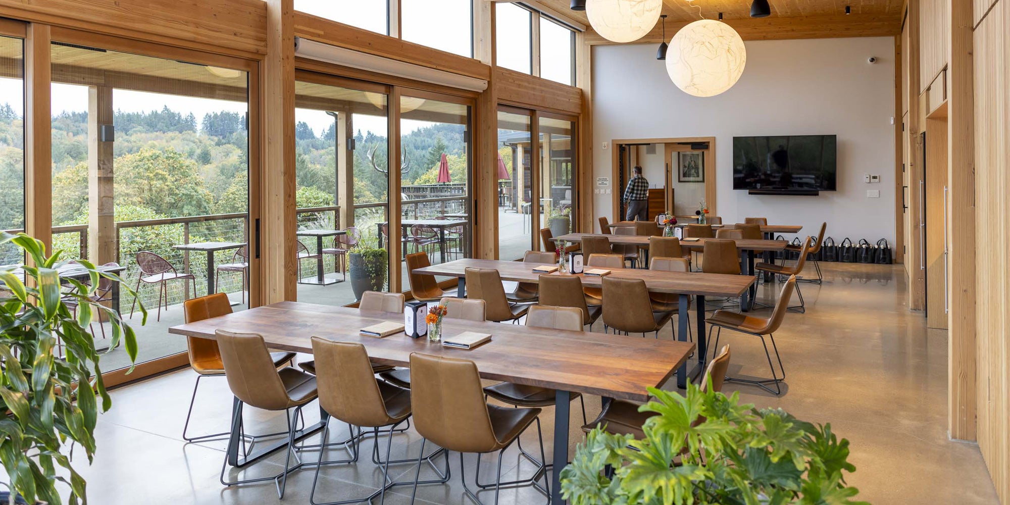 Modern winery, Elk Cove with wooden tables and chairs, large windows, and a TV on the wall.
