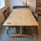 Wooden dining table with four chairs in a room with a lamp and shelves.