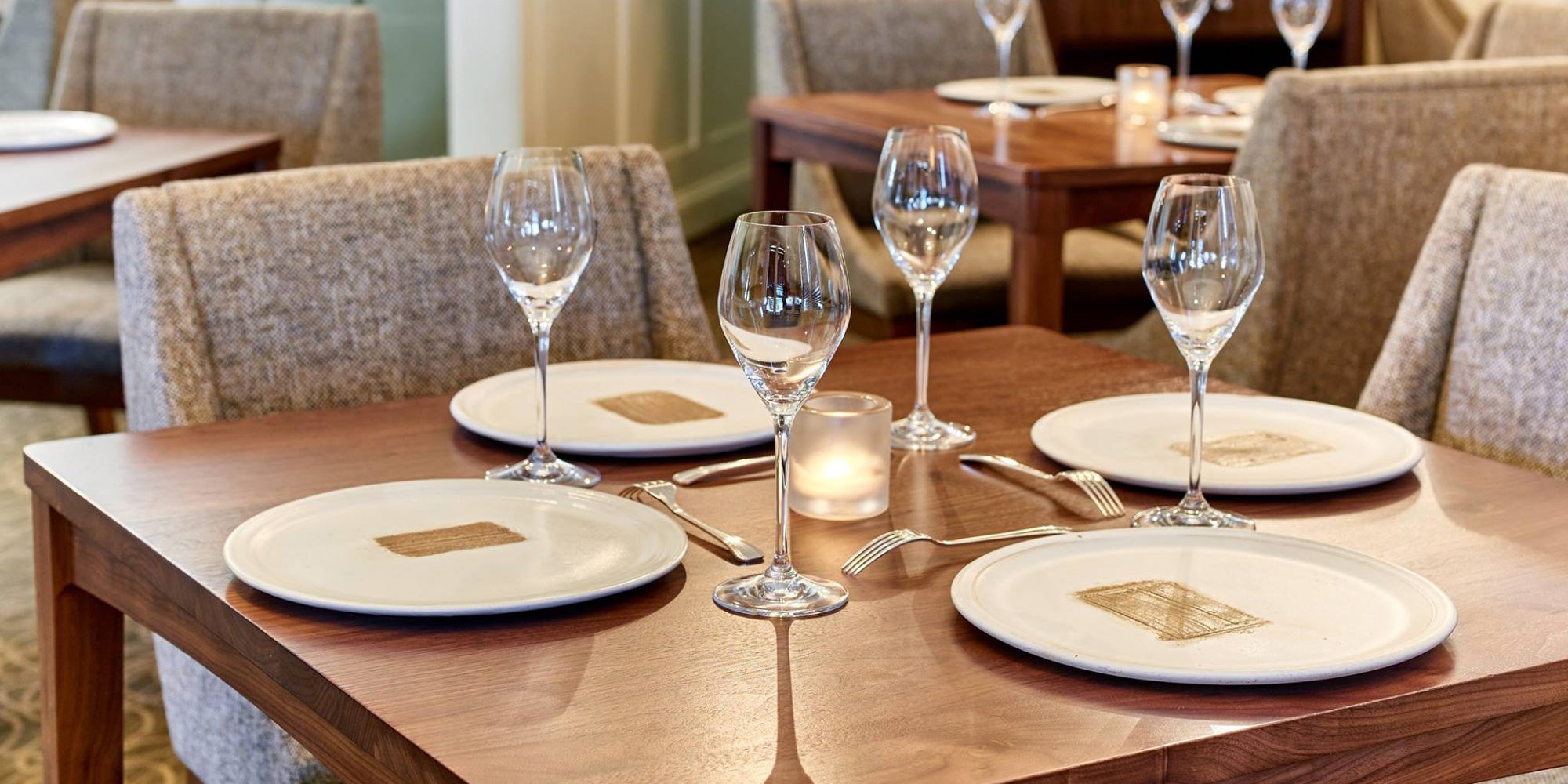 Dining table set with plates, glasses, and candles in a restaurant setting.