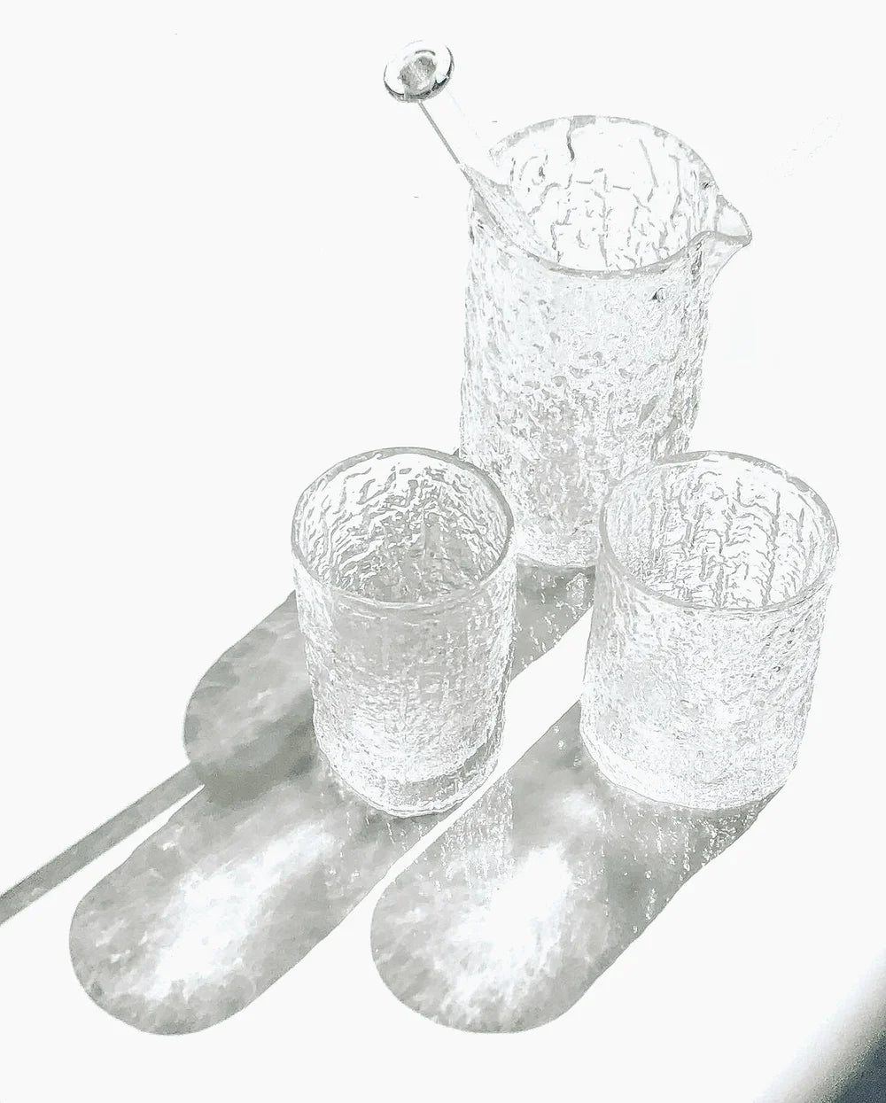 Set of textured glass tumblers and a pitcher on a white background