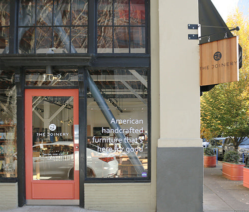 Storefront with glass window displaying interior and promotional text, with a wooden sign above.